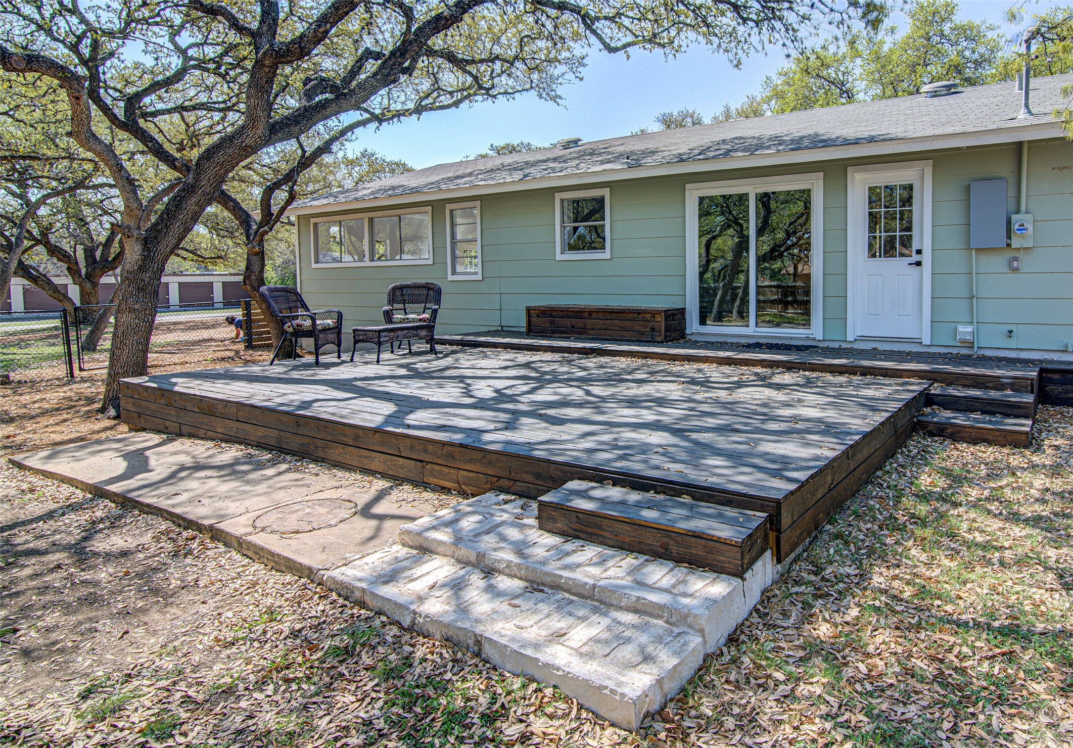 207 Haley Road Johnson City, TX 78636 - Photo 6 of 31 An inviting wood deck extends from the light green siding, perfect for outdoor relaxation under the shade of mature trees.