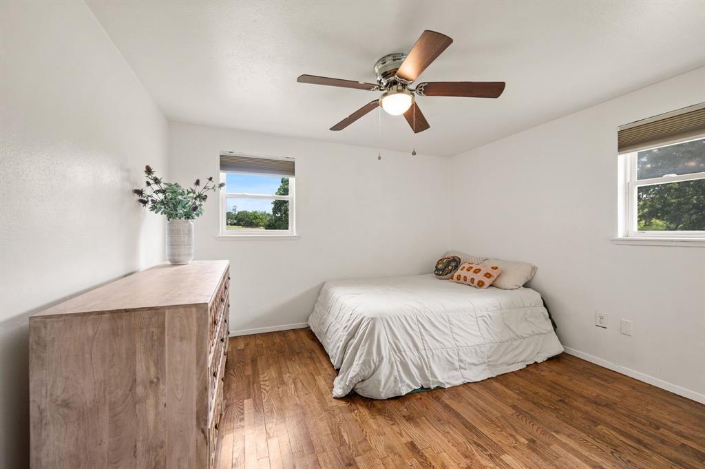 3900 Moseley Road Cross Roads, TX 76227 - Photo 11 of 36 Room featuring wood-finish flooring, two windows with roller shades, and a ceiling fan with integrated lighting