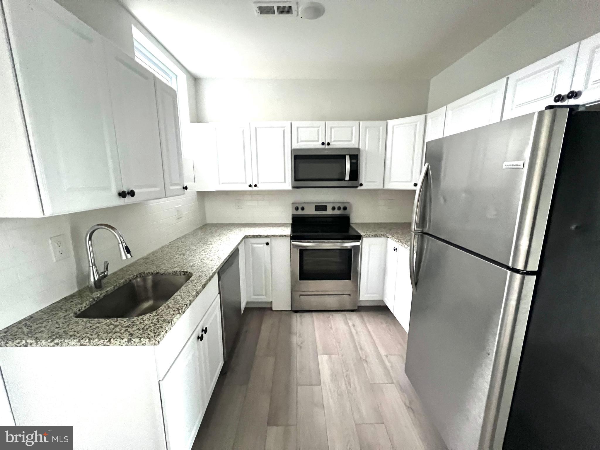 a kitchen with granite countertop a refrigerator sink and white cabinets