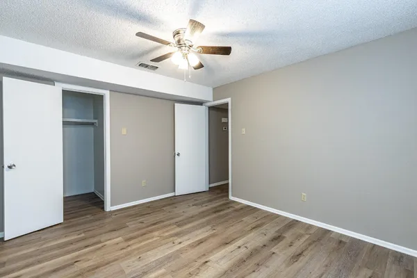 an empty room with wooden floor fan and windows