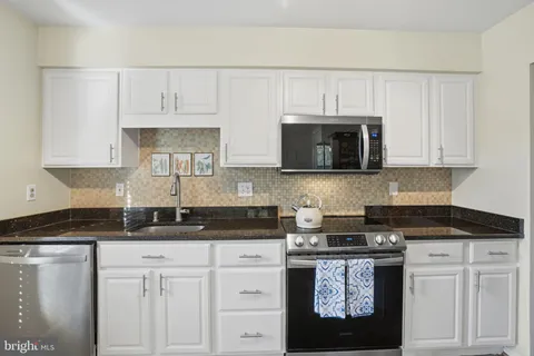 a kitchen with stainless steel appliances granite countertop white cabinets and a stove a sink