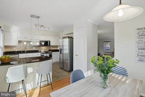 a kitchen with stainless steel appliances granite countertop a refrigerator a sink dishwasher a dining table and chairs with wooden floor