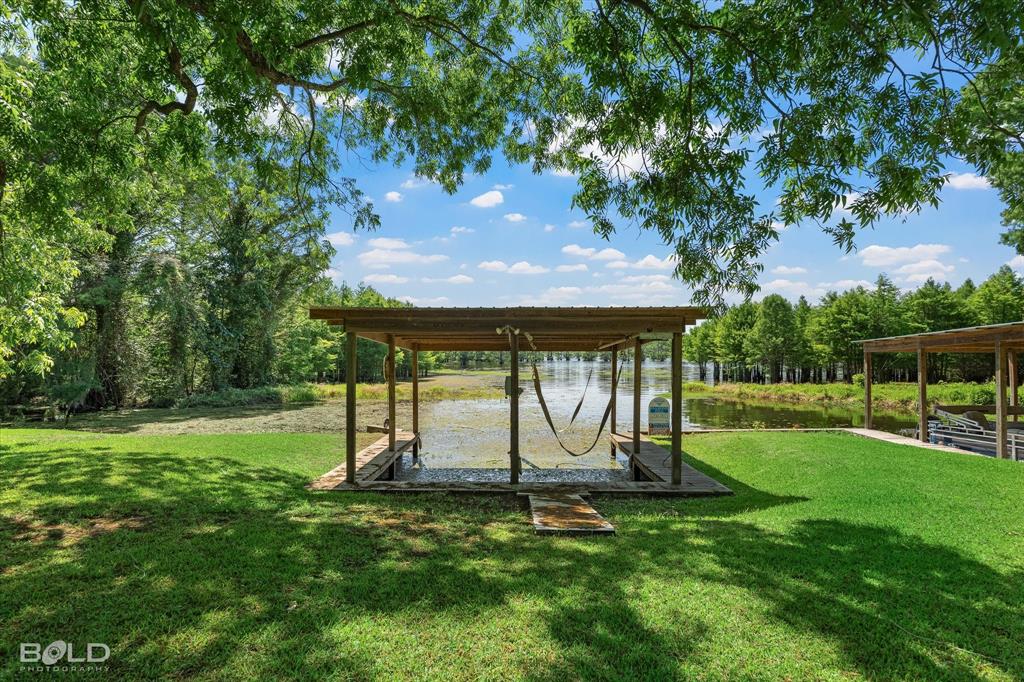 225 Marie Road Ringgold, LA 71068 - Photo 4 of 40 Waterfront property featuring a covered boat dock with a lift, expansive green lawn, mature trees, and direct water access