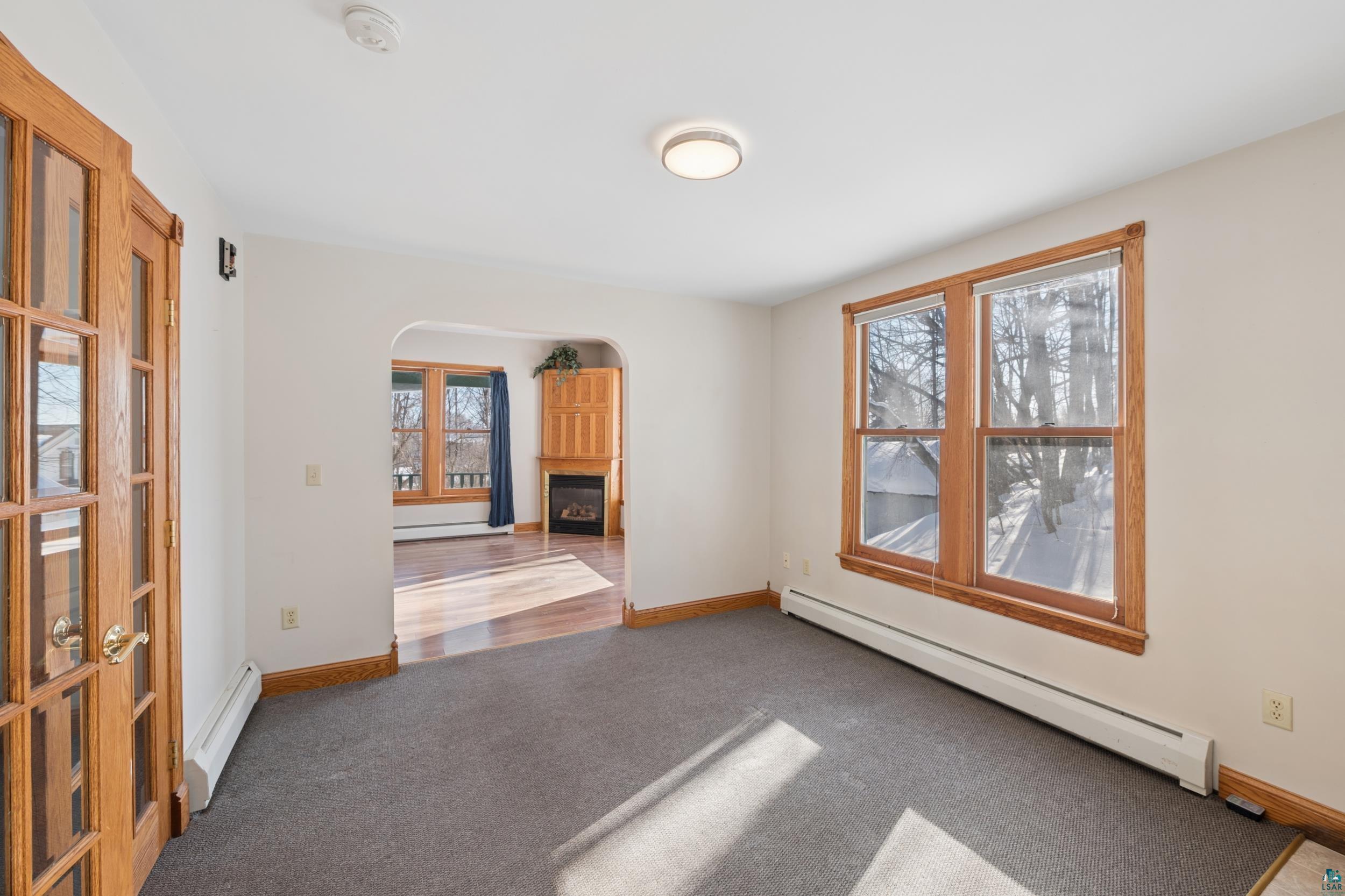 33 South 4th Street Bayfield, WI 54814 - Photo 11 of 29 Carpeted spare room featuring a baseboard heating unit, a glass covered fireplace, arched walkways, and a baseboard radiator