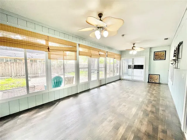 a view of an empty room with wooden floor and a ceiling fan