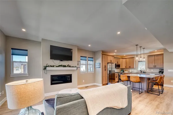 a living room with stainless steel appliances furniture a fireplace a flat screen tv and a kitchen view