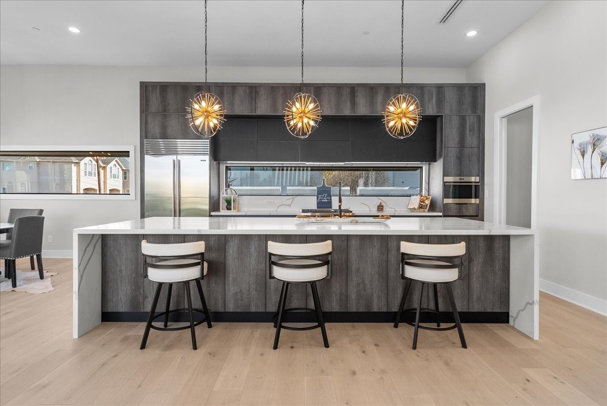 516 Reinerman Street Houston, TX 77007 - Photo 10 of 42 This modern kitchen features a spacious island with seating for three, sleek dark cabinetry, and high-end stainless steel appliances. Elegant pendant lights add a stylish touch, while the open layout connects to the dining area, enhancing the airy feel.