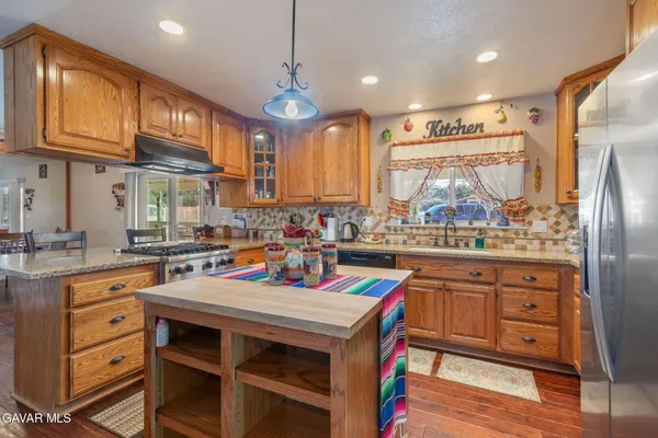 a kitchen with stainless steel appliances granite countertop a stove a refrigerator a sink dishwasher and white cabinets with wooden floor