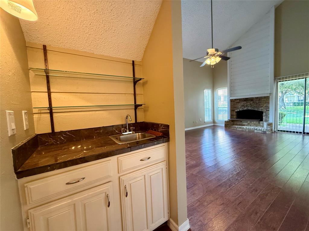777 Custer Road, Unit 23 Richardson, TX 75080 - Photo 23 of 28 Indoor wet bar with a textured ceiling, dark wood finished floors, a stone fireplace, open shelves, and ceiling fan