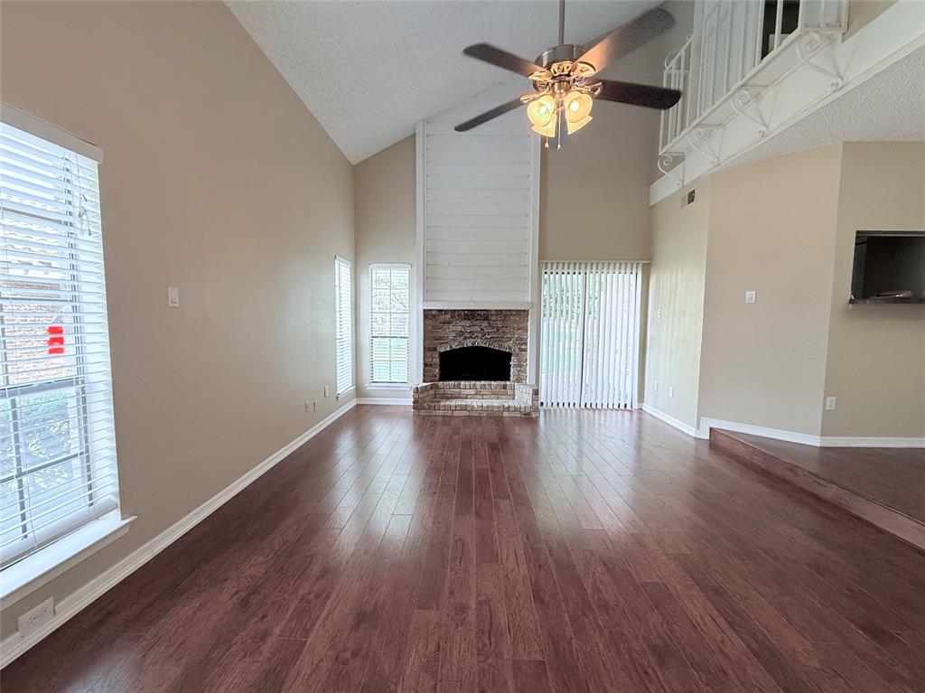 777 Custer Road, Unit 23 Richardson, TX 75080 - Photo 7 of 28 Unfurnished living room featuring high vaulted ceiling, a stone fireplace, dark wood-style flooring, a textured ceiling, and ceiling fan