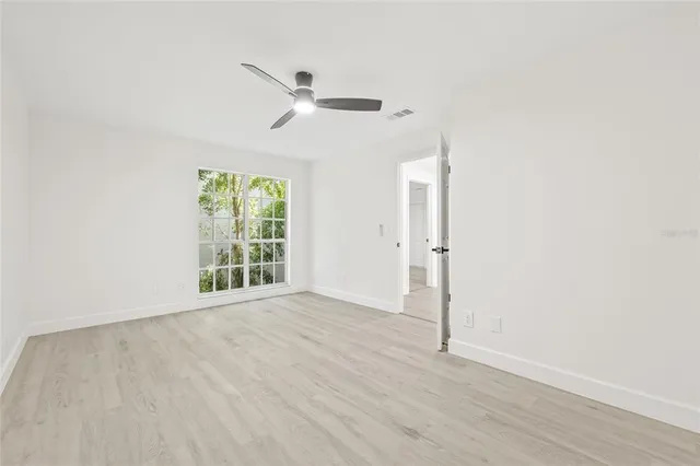 an empty room with wooden floor fan and windows