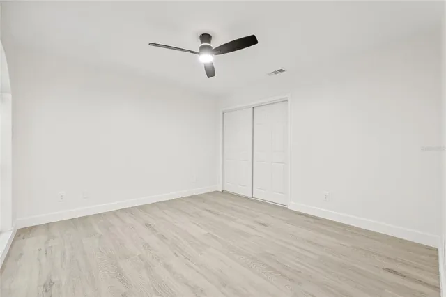 an empty room with wooden floor ceiling fan and windows