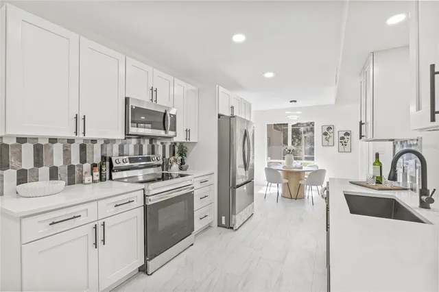 a kitchen with stainless steel appliances a sink a stove a refrigerator cabinets and a dining table