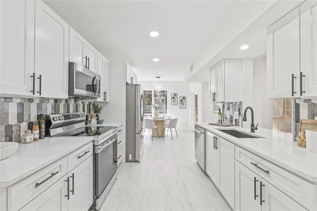 a large white kitchen with stainless steel appliances lots of counter space and a sink