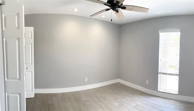 an empty room with wooden floor fan and windows