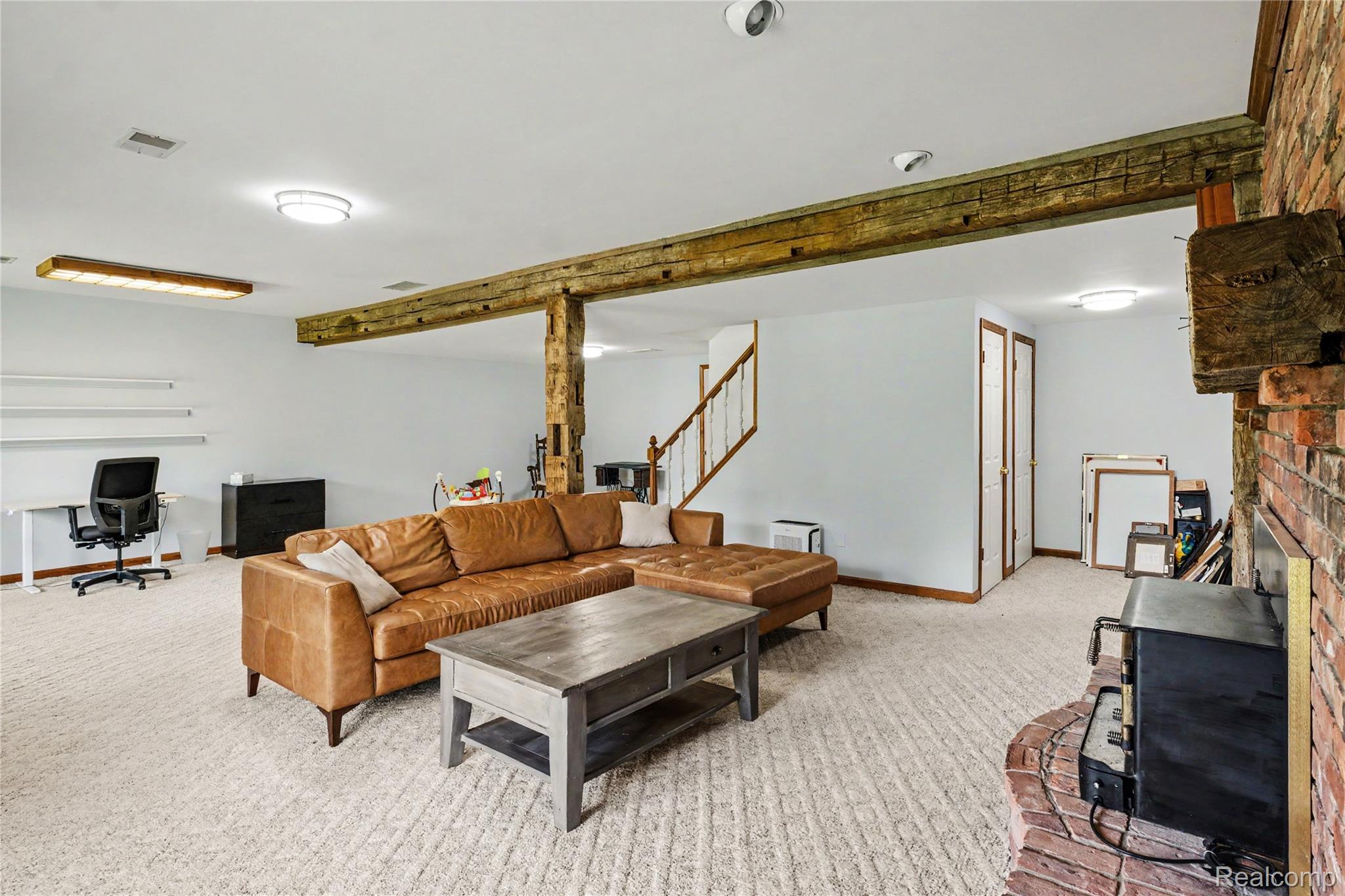 5465 South Lake George Road Metamora, MI 48455 - Photo 33 of 61 Spacious room featuring exposed wood beams, a brick fireplace, light-colored carpeting, multiple light fixtures, and a staircase with wood railings