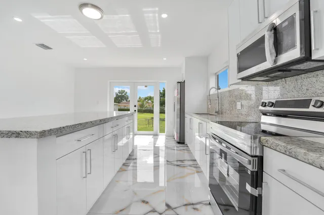 a large white kitchen with stainless steel appliances granite countertop a lot of counter space and wooden floors