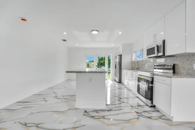 a kitchen with stainless steel appliances kitchen island granite countertop a stove a sink and white cabinets
