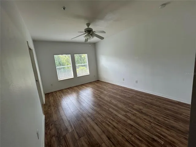 an empty room with wooden floor chandelier fan and windows