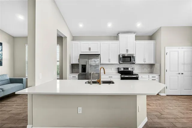 a kitchen with stainless steel appliances a sink a stove a refrigerator white cabinets and wooden floor