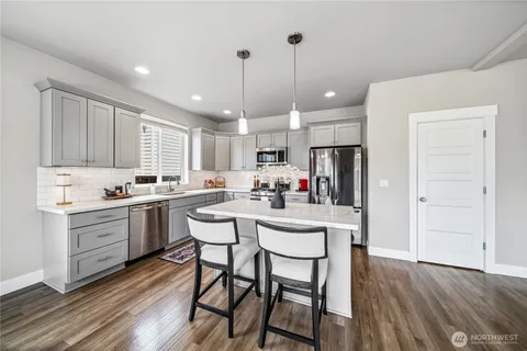 a kitchen with stainless steel appliances kitchen island granite countertop a stove a sink a refrigerator and white cabinets with wooden floor