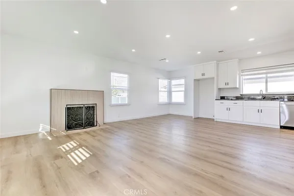 a view of a kitchen and empty room with wooden floor fireplace and windows