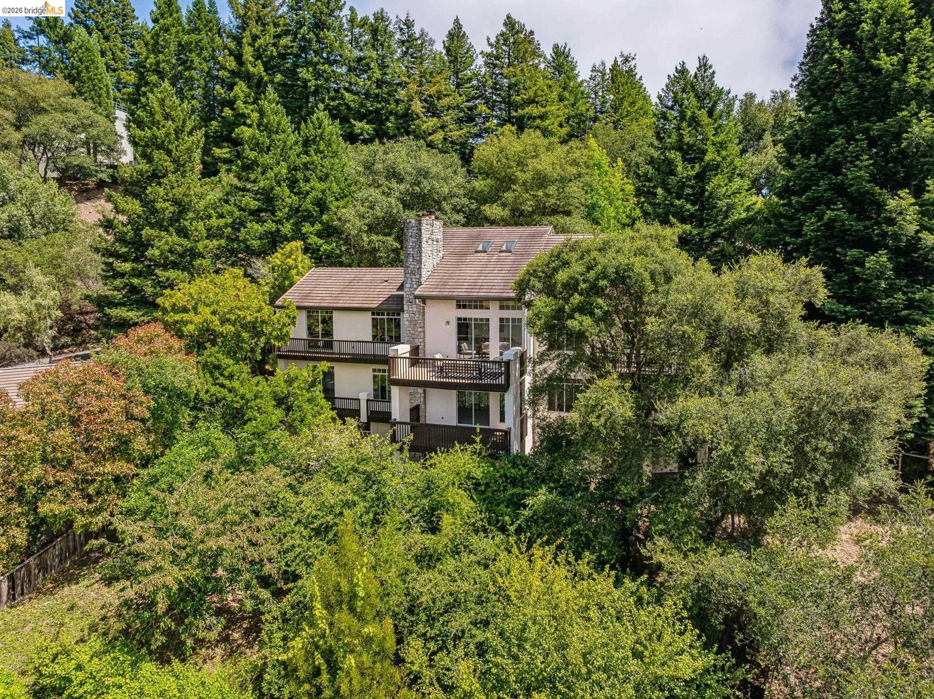 1325 Drury Road Berkeley, CA 94705 - Photo 3 of 71 Multi-level residence featuring a stone chimney, multiple balconies, and a dark tile roof, surrounded by mature trees