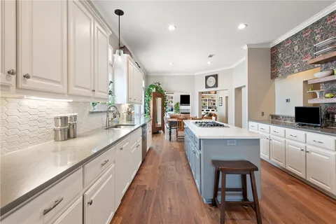 a large white kitchen with cabinets a sink dishwasher a stove and a dining table with wooden floor