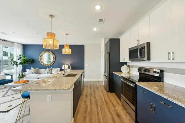a living room with couches a kitchen island with wooden cabinets and stainless steel appliances
