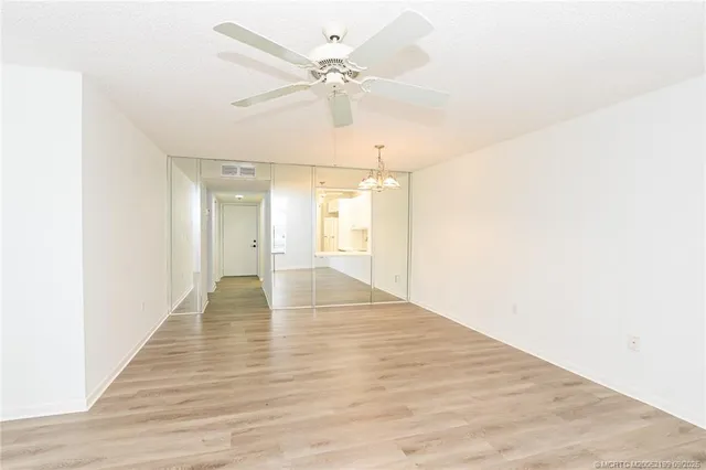 a view of an empty room with wooden floor and a ceiling fan