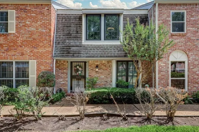 a view of a brick house with plants and large tree