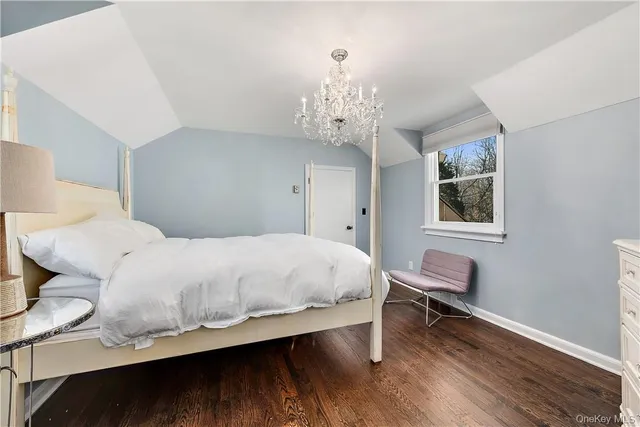 a bedroom with a bed table chair chandelier and a window