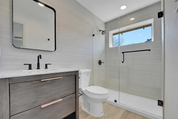 a bathroom with a toilet a sink a glass door a shower a mirror and vanity
