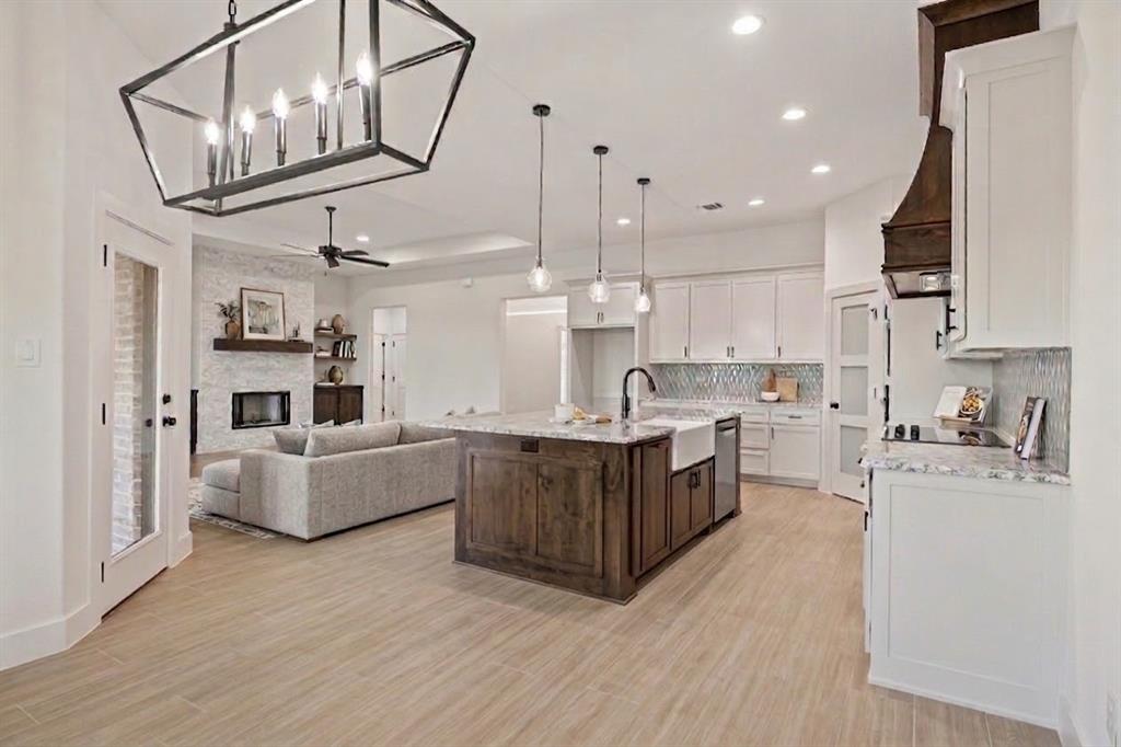 8017 Rnch Vw Place Springtown, TX 76082 - Photo 10 of 18 Wood-finish flooring throughout, kitchen island with built-in cabinetry, white shaker cabinetry, mosaic tile backsplash, and a fireplace with a stone surround