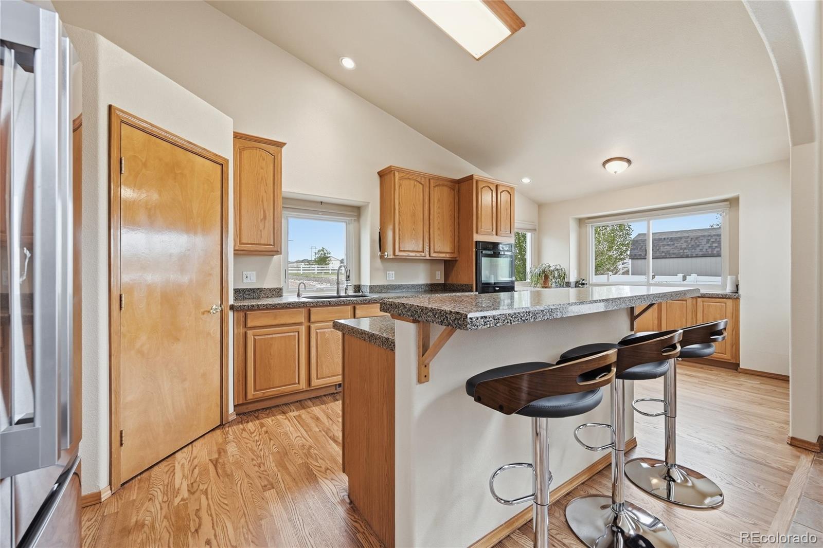 9288 Rockingham Drive Peyton, CO 80831 - Photo 12 of 49 a kitchen with stainless steel appliances granite countertop a refrigerator a stove a sink a dining table and chairs with wooden floor