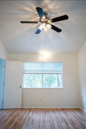an empty room with wooden floor fan and windows