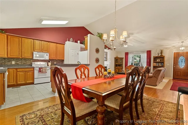 a dining room with furniture a kitchen a chandelier and wooden floor