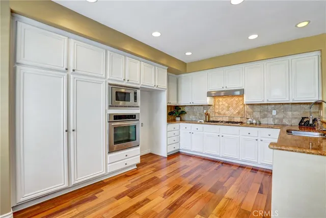 a kitchen with granite countertop wooden floors stainless steel appliances and white cabinets