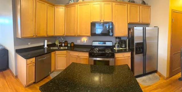 a kitchen with stainless steel appliances granite countertop a refrigerator a stove and a sink with wooden floor