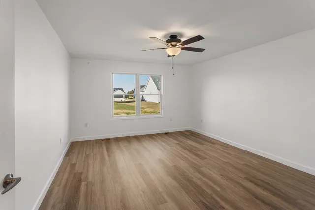 an empty room with wooden floor chandelier fan and windows