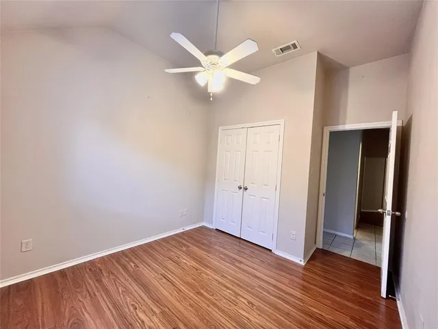 a view of an empty room with wooden floor and a ceiling fan