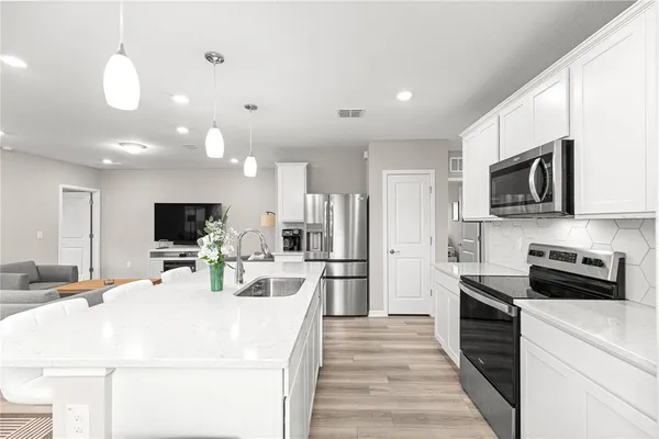 a kitchen with stainless steel appliances a stove top oven a refrigerator a sink and white cabinets with wooden floor