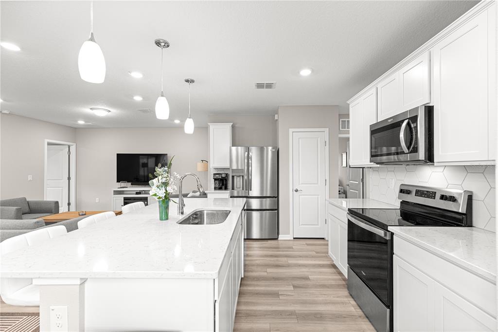 5466 Southwest 85th Ave Road Ocala, FL 34481 - Photo 8 of 36 a kitchen with stainless steel appliances a stove top oven a refrigerator a sink and white cabinets with wooden floor