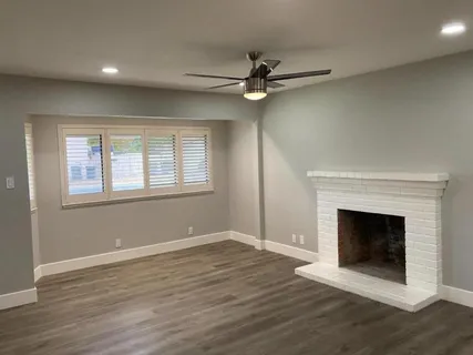 a view of an empty room with wooden floor fireplace and a window