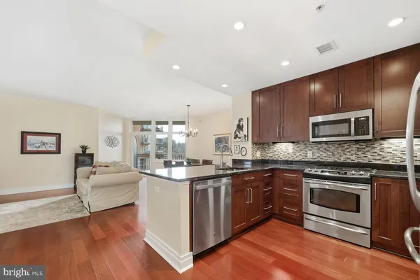 a kitchen with stainless steel appliances granite countertop wooden cabinets a sink a stove a dining table and chairs