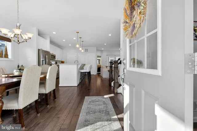 a living room with couches chandelier and a dining table with wooden floor