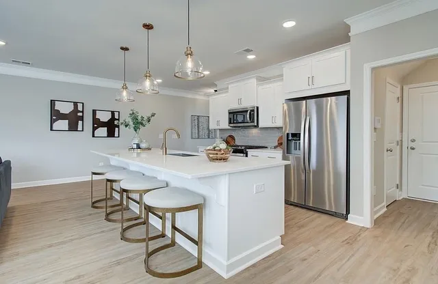 a kitchen with stainless steel appliances granite countertop a refrigerator a oven a sink a stove a dining table and chairs with wooden floor