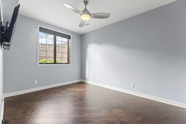 an empty room with wooden floor ceiling fan and windows