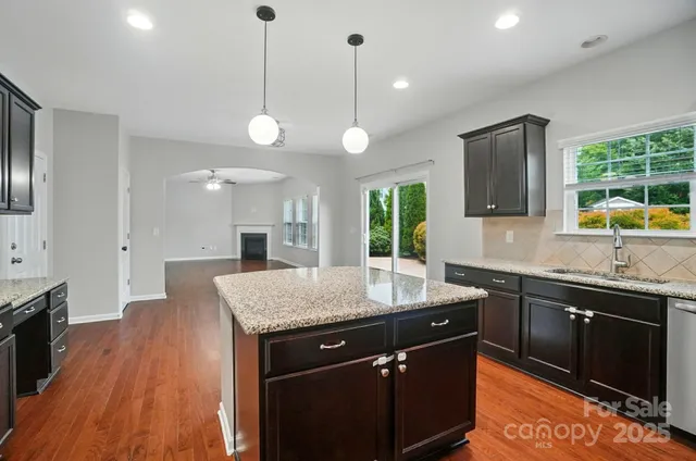 a kitchen with stainless steel appliances granite countertop wooden cabinets a stove a sink a window and wooden floor