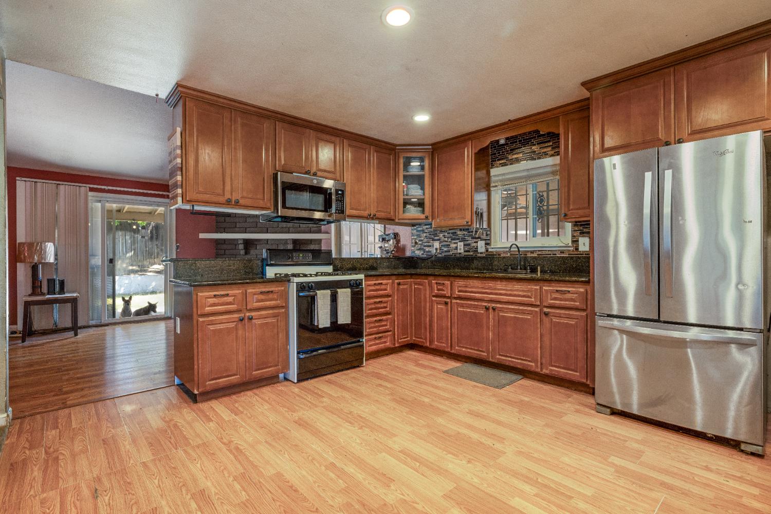 808 Cadillac Drive Modesto, CA 95351 - Photo 8 of 41 kitchen featuring stainless steel microwave, wood finish cabinets, recessed lighting, light wood-type laminate flooring, and dark stone counters